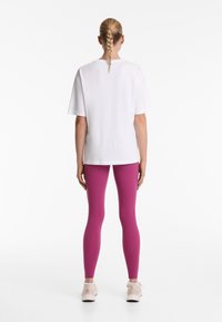 Hvid bomulds t-shirt med korte ærmer, parret med lyserøde leggings med en glat tekstur og en tætsiddende form, afsluttet med lette sneakers.