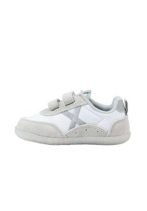 Zapatilla blanca con acentos de ante gris, correas de gancho y bucle, y puntera redondeada. Presenta una suela texturizada y un diseño prominente en forma de "X".