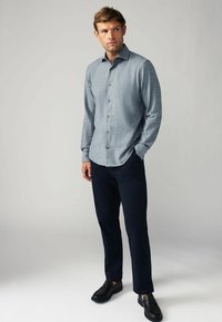 Hellblaues Hemd mit langen Ärmeln, kombiniert mit marineblauen Hosen und schwarzen Schuhen; glattes Material und ein lässiges, tailliertes Design.