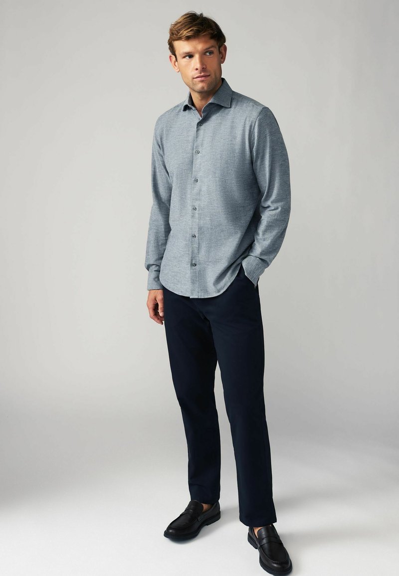 Hellblaues Hemd mit langen Ärmeln, kombiniert mit marineblauen Hosen und schwarzen Schuhen; glattes Material und ein lässiges, tailliertes Design.