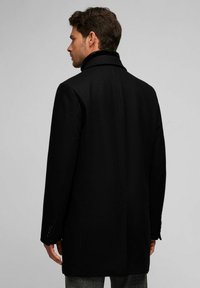 Abrigo de lana negro con un alto cuello, forma entallada y puños abotonados. Presenta una espalda recta y dos bolsillos laterales.