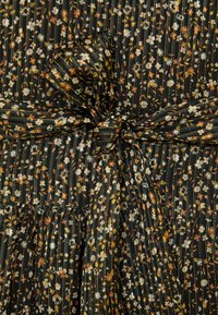 Črna tkanina z majhnim belim, oranžnim in rumenim cvetličnim vzorcem, ki vključuje navpične kovinske zlate proge, zavezana v pentljo na pasu.