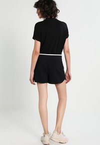 Top negro de manga corta y pantalones cortos negros a juego con una banda blanca en la cintura; tejido suave y corte relajado. Calzado casual de color claro.