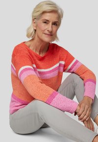 Gestrickter Pullover mit horizontalen Streifen in Orange, Pink und Weiß, strukturiertem Stoff und V-Ausschnitt, kombiniert mit hellgrauen Hosen.