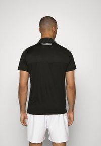 Svart polo skjorta med en texturerad bakpanel, med krage och korta ärmar. Lacoste-logotypen är synlig vid nacken.