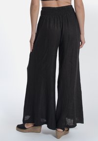 Pantaloni palazzo neri, fluidi e realizzati in tessuto leggero, con vita alta arricciata e gambe ampie, mostrati da dietro.