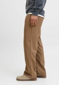 Brown tailored pants made of soft fabric, featuring a straight-leg cut. Worn with a grey sweater and beige footwear. Minimalist design.