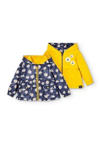 Deux vestes réversibles pour enfants avec capuches ; une jaune avec des imprimés de marguerites, l'autre bleu marine avec des motifs de marguerites blanches et une fermeture éclair jaune.
