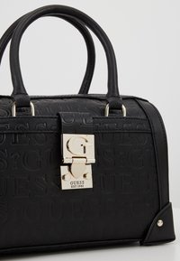 Zwarte leren handtas met reliëf logo patroon, dubbele handgrepen en een goudkleurige sluiting met logo detail. Gestructureerde vorm en zilveren accenten.