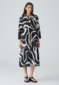 Schwarz-weiß gemustertes Kleid mit langen Ärmeln und schichtedem Design; verfügt über einen Kragen und eine Knopfleiste, gefertigt aus leichtem Stoff.