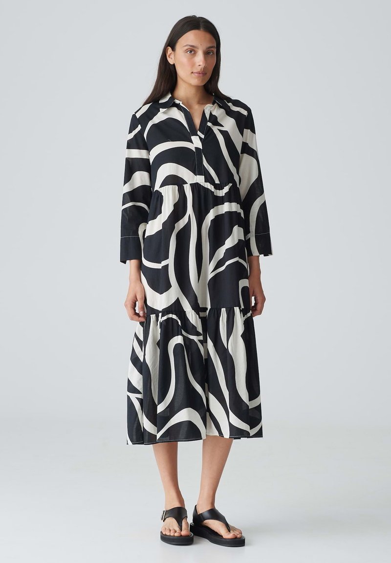 Schwarz-weiß gemustertes Kleid mit langen Ärmeln und schichtedem Design; verfügt über einen Kragen und eine Knopfleiste, gefertigt aus leichtem Stoff.