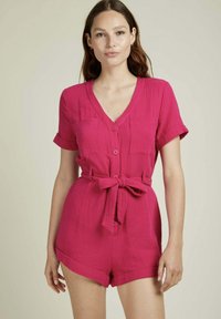Combinaison rose à manches courtes avec un décolleté en V, devant boutonné, deux poches poitrine et une ceinture nouée à la taille. Tissu texturé avec un design décontracté.