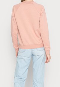 Ljusrosa sweatshirt med ribbade muddar och nederkant, raglanärmar och mjuk textur. Buren med ljusblå, löst sittande jeans.