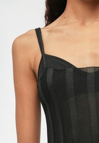 Musta hihaton paita ohuilla olkaimilla, valmistettu teksturoituneesta neulekankaasta, jossa on pystysuorat raidat ja slim fit -malli. Koristeena on läpikuultava paneeli.