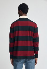 Langarm-Polohemd mit horizontalen roten und schwarzen Streifen, cremefarbenem Kragen und lockerem Schnitt. Hergestellt aus weichem, strukturiertem Stoff.