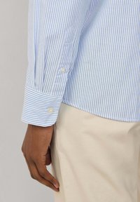Camicia a righe blu chiaro e bianco con polsini abbottonati, realizzata in cotone, caratterizzata da una texture morbida e un design colletto classico.