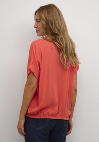 Haut corail à manches courtes en forme de chauve-souris, en tissu texturé, coupe décontractée et ourlet élastiqué ; associé à un jean bleu marine.