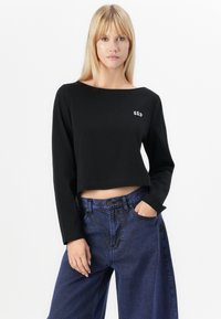 Black cropped long-sleeve top with a wide neckline and white "GAP" logo. Paired with high-waisted light blue wide-leg jeans.