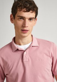 Svetlo roza polo majica iz bombaža, z ovratnikom, trima gumbi in majhnim vezenim logotipom na prsih.