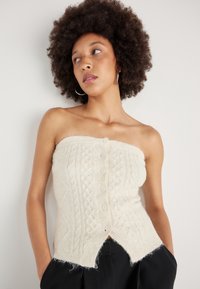 Top strapless em malha canelada creme com frente de bot�ões, padrão texturado e bainha desfalcada. Usado com calças escuras, tecido leve e design ajustado.