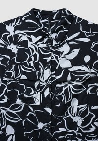 Kurzärmliges, schwarzes Hemd mit weißem Blumenmuster, mit einem Kragen und zwei vorderen Taschen. Hergestellt aus leichtem, glattem Stoff.