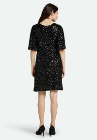 Vestido negro con lentejuelas, de mangas cortas y escote redondo, con un corte suelto y un dobladillo a la altura de la rodilla, combinado con tacones altos negros.