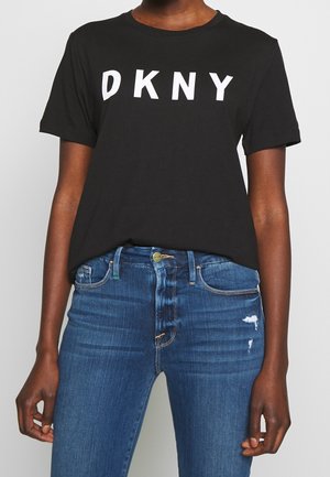 Black cotton t-shirt with "DKNY" in bold white letters on the front. Short sleeves and relaxed fit. Paired with blue distressed jeans.
