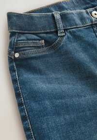 Közelkép kék farmernadrágról, amelyen látható a derékpánt, övbuc, a hátsó zseb, a kis érmezseb, a kontrasztos varrás és a fémtár. 