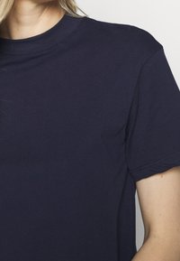 Mørkeblå bomulds t-shirt med klassisk rund halsudskæring, korte ærmer, glat tekstur og subtil syning ved kanten og ærmerne.