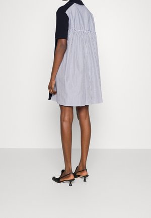 Femme debout portant une robe courte rayée noir et blanc à manches courtes et des chaussures à talons petits noirs avec bride arrière.