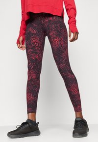 Sorte og røde mønstrede tights med tettsittende passform, med en glitrende finish og kontrasterende sømmer. Kombinert med svarte joggesko.