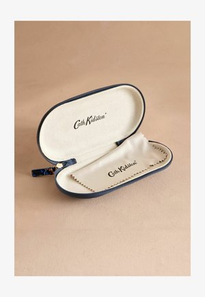 Tvrdi etui za naočale od tamnoplave tkanine s zatvaranjem na zip. Unutrašnjost sadrži bež postavu, otisnutu oznaku i krpicu za čišćenje sa cik-cak rubovima.