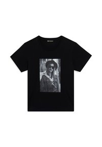 T-shirt in cotone nero con una stampa grafica frontale di una donna con occhiali da sole, accompagnata dal testo "IL MOVIMENTO È UNA TERAPIA" in grassetto. Maniche corte.