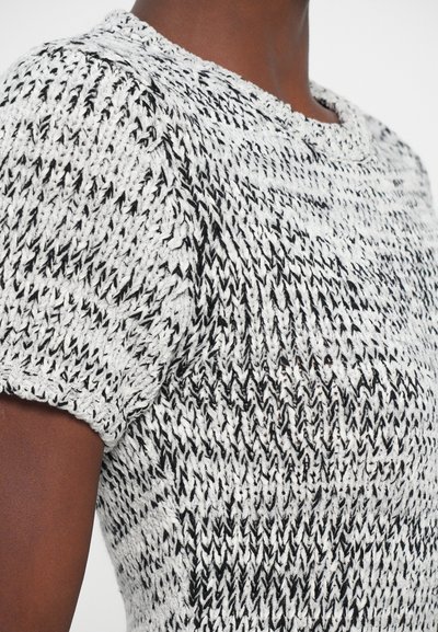 Primo piano di una persona che indossa un maglione a maglia testurizzata bianco e nero a maniche corte con scollatura rotonda.