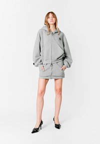 Sudadera gris con cremallera y mangas oversize, acompañada de una falda a juego. Ambos presentan un tejido suave y un diseño minimalista.