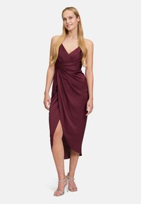 Bordowa sukienka z dekoltem w serek, marszczonym w pasie i rozcięciem z przodu. Wykonana z gładkiego materiału, zestawiona z sandałami na obcasie w kolorze srebrnym.