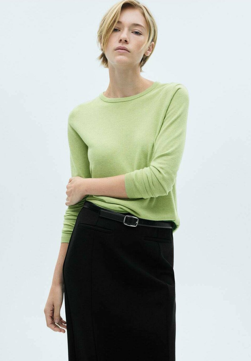 Svetlo zelena dolga rokava pulover s okroglo izrezom v kombinaciji s črno krilo, ki ima pas in žepi. Gladka tekstura, sproščen kroj.