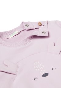 Suéter de bebé en color lila con cierres de botones y snaps en el cuello, que presenta una bonita cara de oso y orejas de tela en la parte frontal.