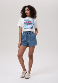 Λευκό μπλουζάκι με μπλε ρίγες και κόκκινο γραφικό της καρδιάς, συνδυασμένο με ανοιχτό μπλε τζιν σορτσάκι, που διαθέτει ελαστική μέση και τσέπες.