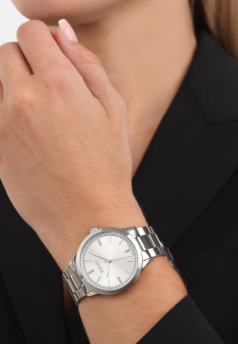 Srebrny zegarek metalowy z okrągłą tarczą i g�ładką białą cyferblatą. Posiada kryształowe akcenty wokół obręczy oraz wypolerowaną bransoletę.