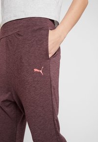 Weinrote Sporthosen mit glatter Textur, die eine Seitentasche und ein pinkes Puma-Logo am Oberschenkel aufweisen.