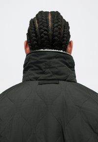 Giacca nera trapuntata con colletto alto e fodera bianca, caratterizzata da un tessuto testurizzato e delicati motivi a onde sulla superficie.