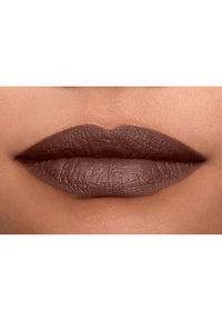 Matte bruine lippenstift aangebracht op volle lippen met zichtbare textuur, die een gladde afwerking en gedefinieerde randen toont tegen een achtergrond van een natuurlijke huidtint.