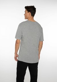 Grijze katoenen t-shirt met een ronde halslijn, korte mouwen en een relaxte pasvorm. Gemaakt met zwarte broek, getoond vanuit een achteraanzicht.