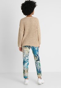 Beige pletený svetr s volným střihem a kulatým výstřihem, doplněný o barevné kalhoty slim fit s mapovým vzorem a bílé tenisky.