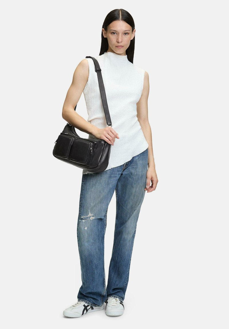 Top bianco senza maniche, jeans azzurri chiari strappati e borsa a spalla nera in pelle con due tasche frontali, abbinata a sneakers bianche.