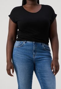 Svart kortärmad topp med spetsdetaljer och figurnära design, kombinerad med blå högmidjade jeans med standardfickor och denimtextur.