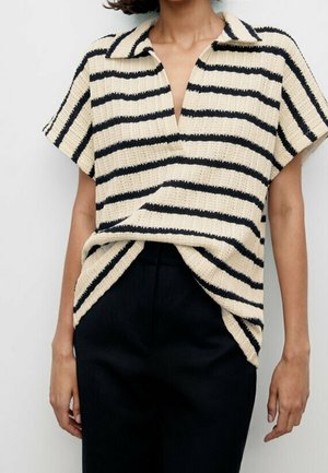 Vrouw draagt een crèmekleurige korte mouw gebreide top met zwarte horizontale strepen, ingestopt in een zwarte hooggetailleerde broek.