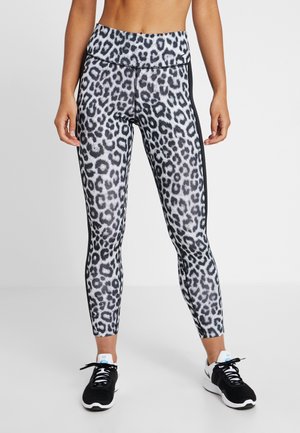 Leggings en imprimé léopard noir et blanc avec une taille haute, dotées de bandes latérales noires, associées à des chaussures de sport noires.