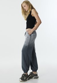 Zwarte cropped tanktop gecombineerd met grijze ombre joggers met zijzakken en drukknoopjes bij de onderbenen. Getextureerd, losse pasvorm.